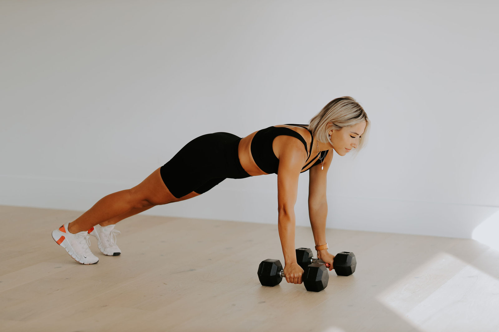 Renegade rows with dumbbells on a pale wood floor in a bright living room.