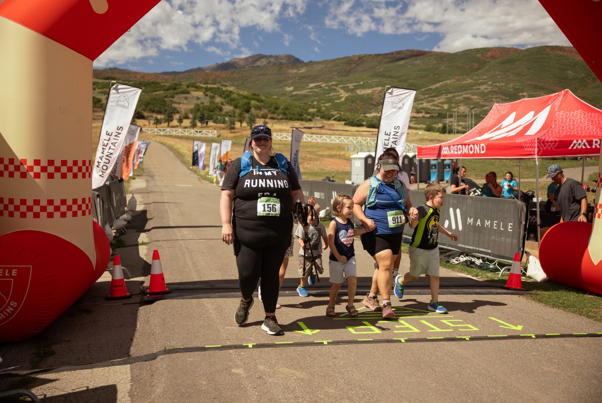 A mom crossing the Mamele Mountains finish line hand in hand with her three young kids under the orange arch.